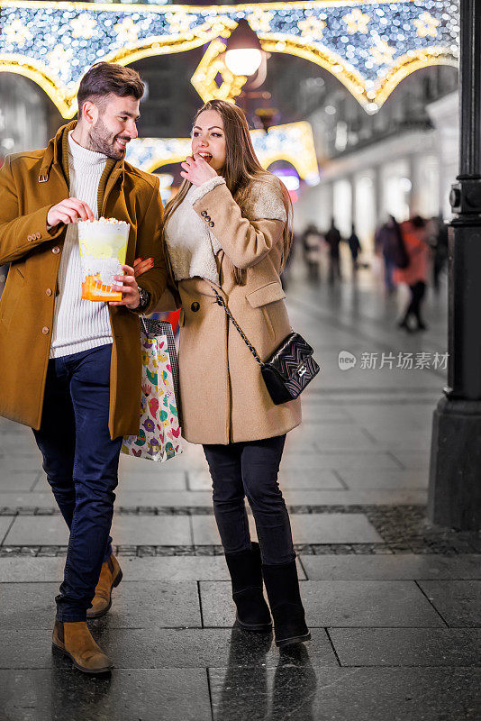 一个快乐的男人和女人在一个寒冷的秋夜走在街上，吃着爆米花。