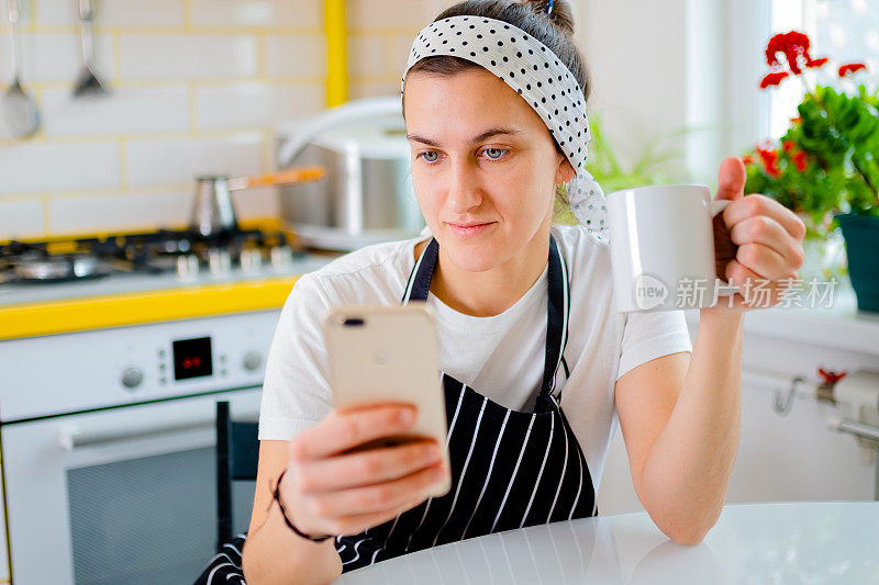 女人坐在桌子旁，用智能手机看新闻，在厨房放松时聊天。放松的概念