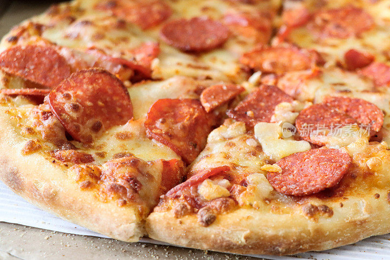 全帧图像的切片意大利辣香肠披萨在纸板外卖披萨盒，融化的金色水牛马苏里拉奶酪和丰富的番茄番茄沙司，重点在前景
