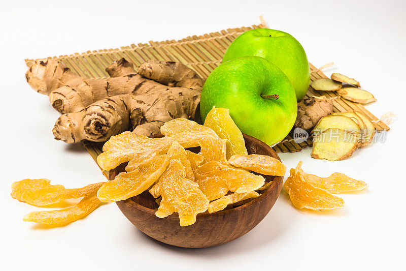 干姜片和糖放在木碗里，新鲜的姜根和绿苹果在白色的背景上。生姜产品具有复制空间。