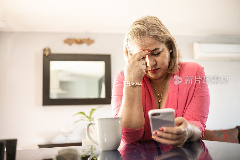 忧心忡忡的成熟拉丁女人在家里使用智能手机