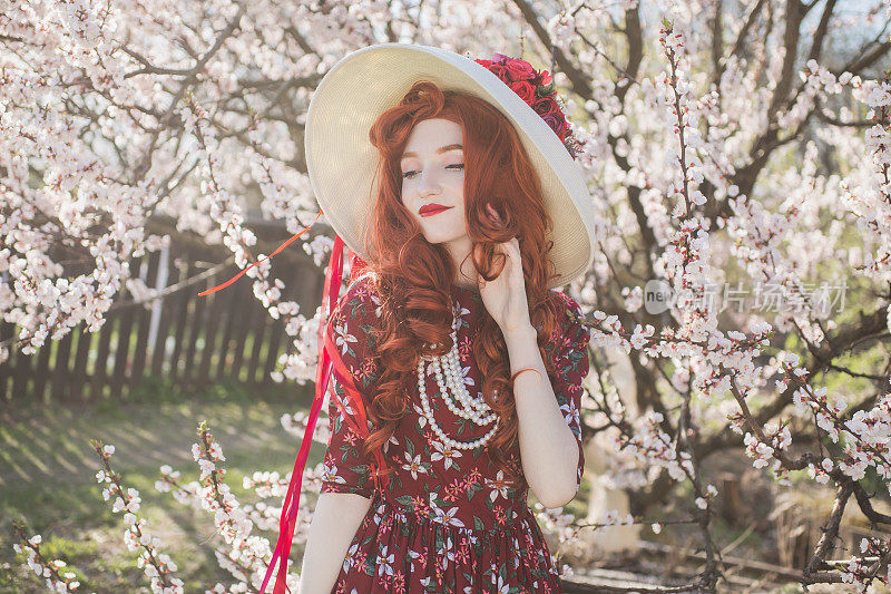 长红头发的女人在春天的树上欣赏盛开的花朵。美丽的红发女孩喜欢简单的事情。健康和自我保健。花的气味。香草味的衣服。樱桃的花园。心理健康