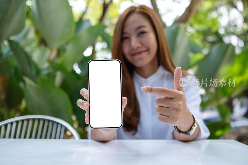 一个年轻女人拿着一个空白屏幕的手机，用手指指着它