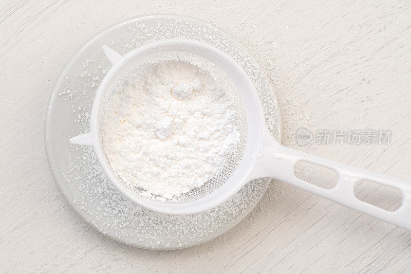 将糖粉放入塑料筛内，置于白色陶瓷板上方。