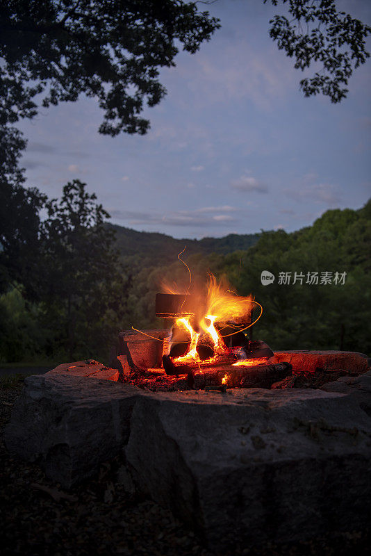 长时间暴露的夜晚篝火的火焰和弯曲的余烬使一个轻的路径与烟雾山天际线的背景