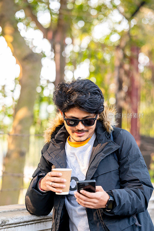 年轻人在冬天喝茶或咖啡，使用智能手机
