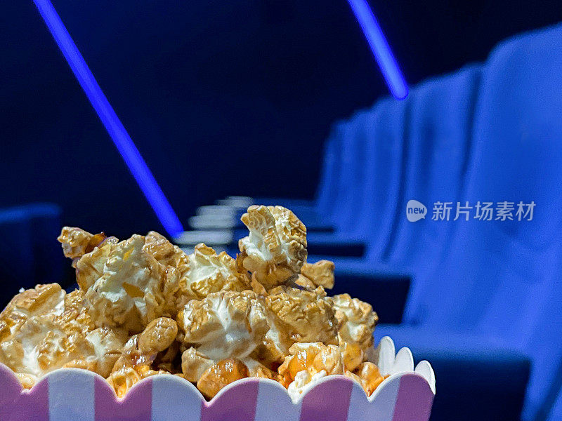 近距离图像的纸箱爆米花在电影院电影院座位，电影零食食品浴缸，蓝色天鹅绒座椅，重点在前景