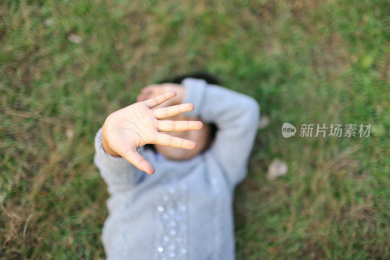 小女孩躺着，捂着脸，手背在草地上