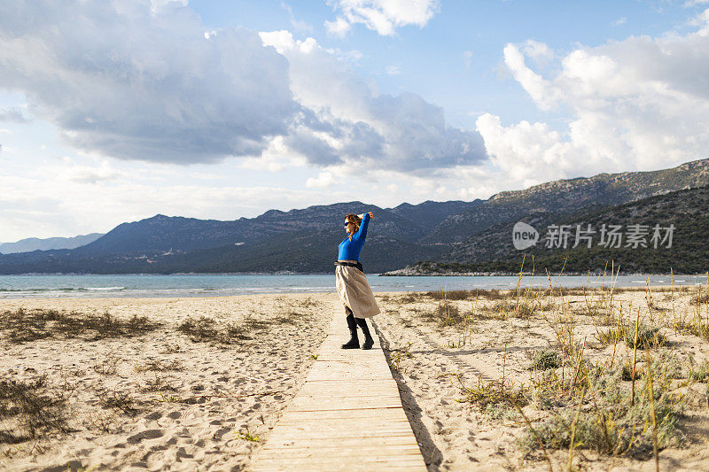 穿着长裙的年轻女子走在海滩上