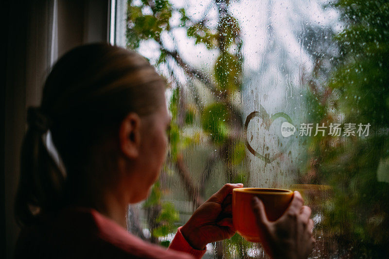 一个女人在雨天喝咖啡，在窗户上画心