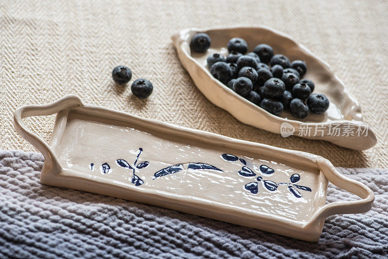 简单的手工陶瓷盘子，新鲜的蓝莓放在棉布桌布上