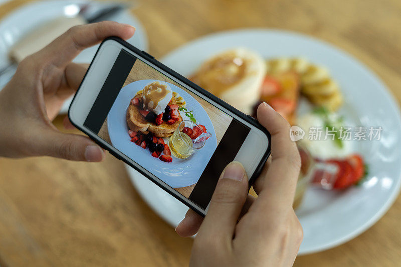 一位女士正在用智能手机给草莓煎饼拍照。女性通过拍照在社交媒体上发布或分享受欢迎的菜肴。