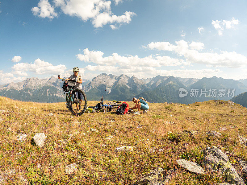 一对夫妇在瑞士阿尔卑斯山骑自行车，日落时分在山顶搭起帐篷