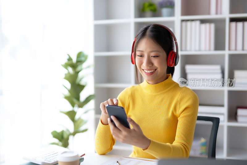 快乐的年轻亚洲女学生戴着耳机在手机上听音乐。