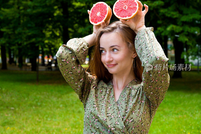 白种快乐的女孩拿着葡萄柚在公园里玩耍。夏天的肖像。维生素