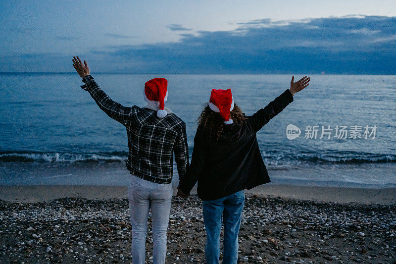 希腊，一对戴着圣诞帽的年轻夫妇在黎明时分欣赏着海岸线的景色