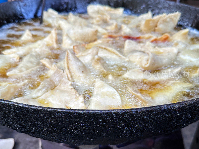 全画幅图像，在karahi(印度锅)中油炸的一批samosas，冒泡的热油，印度街头小吃摊，不健康的饮食，重点放在前景
