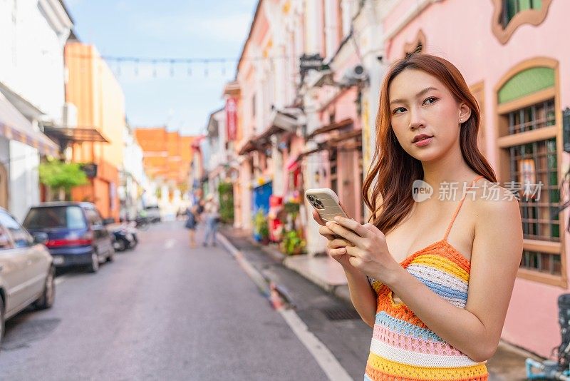 Z世代亚洲女性在旅行中使用智能手机探索普吉岛旧城的魅力，随时随地连接社交媒体。年轻女子与设备互动。通过设备连接生活方式。