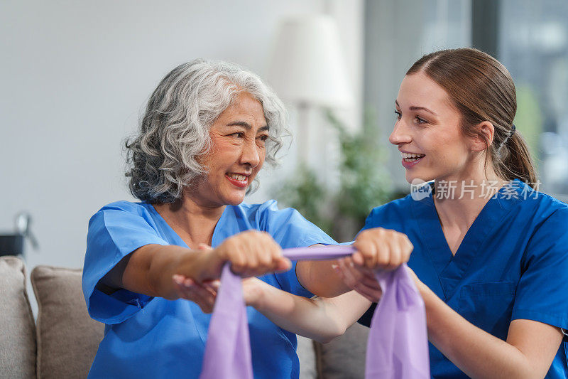 一位年轻的白人物理治疗师和一位60多岁的亚洲老年妇女参加了关于肌肉疼痛和肌肉无力的物理治疗课程。用松紧带让脚后跟疼痛