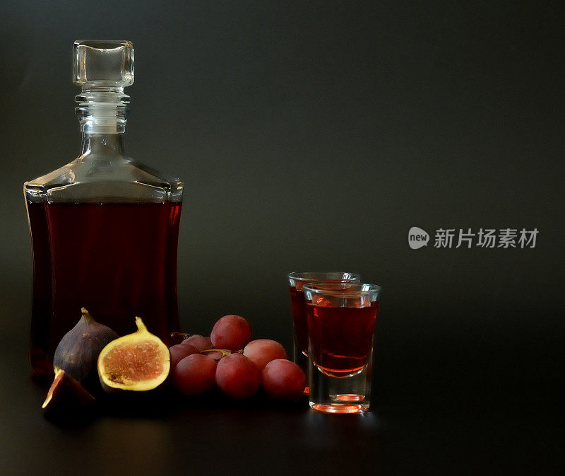 一瓶和两杯无花果葡萄利口酒，黑色背景，旁边是成熟的水果。