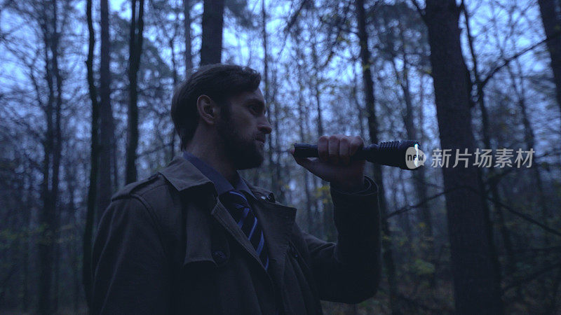 一个拿着手电筒的男人独自在令人毛骨悚然的黑暗森林里游荡，这是一个危险而可怕的地方