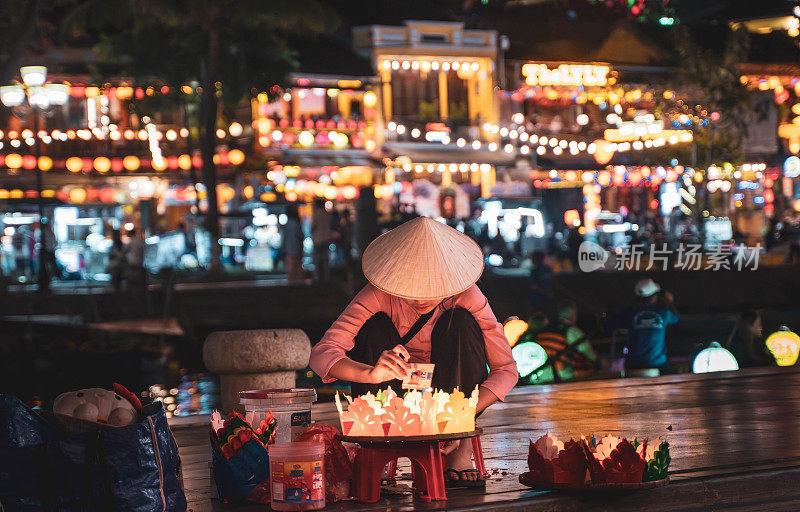 年轻的越南妇女在会安夜市出售传统的蜡烛和灯笼。