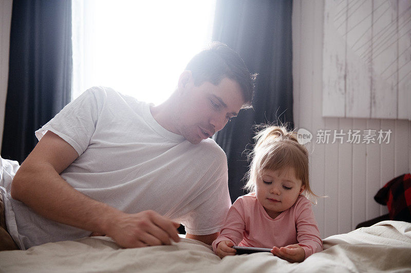 可爱的小女孩在床上和爸爸玩手机