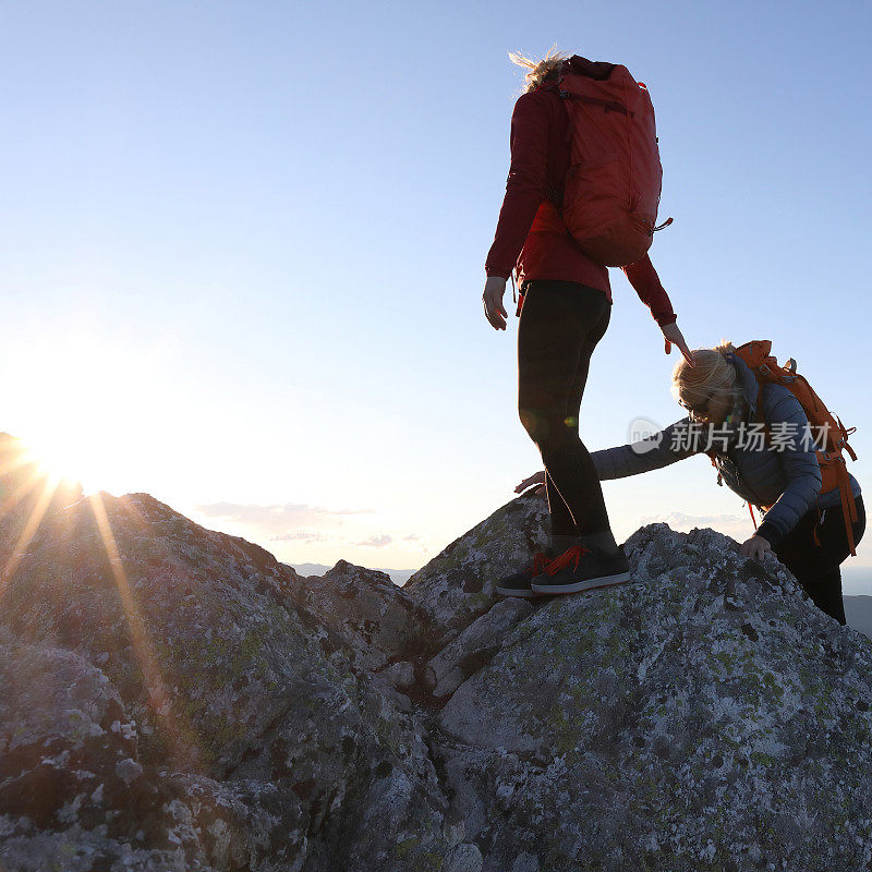 女徒步旅行者在日落时分爬上山顶