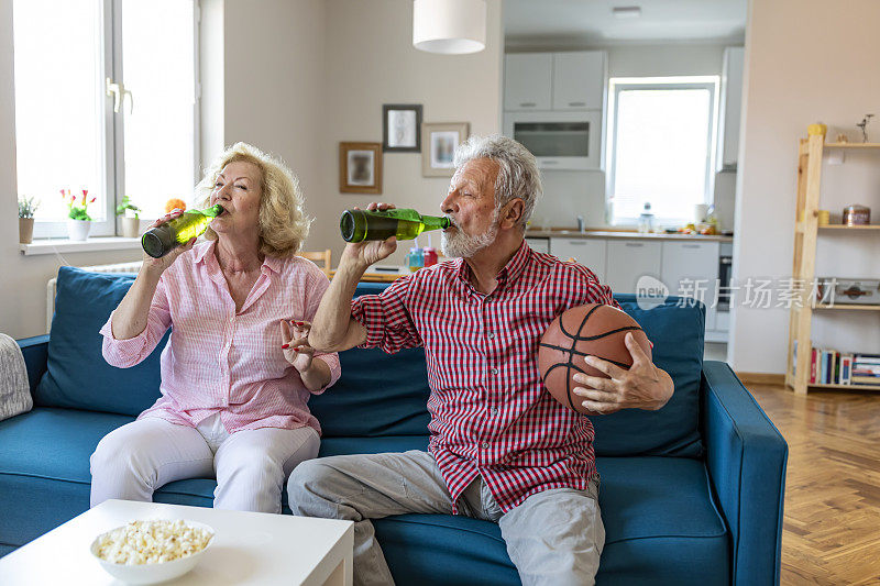 一对成熟的夫妇正在家里的沙发上看篮球比赛。