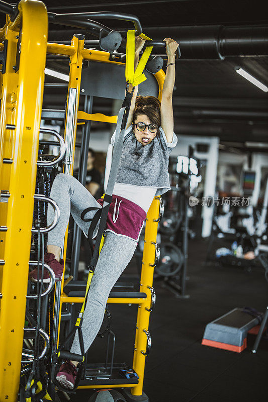 可怕有趣的女运动员在健身房用TRX带子锻炼。