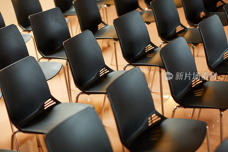 背景图片:在研讨会和培训班的礼堂里，一排排空的黑色塑料椅子