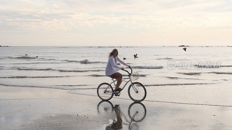日出时分，一名女子骑着自行车沿着热带海滩骑行