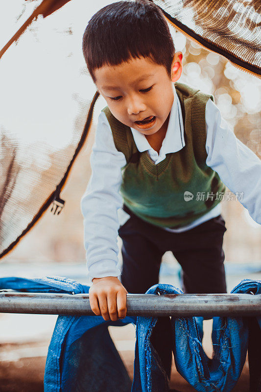 可爱的亚洲幼童有乐趣尝试爬上一个方格架