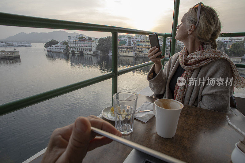 看过去的手在电脑上的女人用手机拍照从一个户外咖啡馆上面的湖