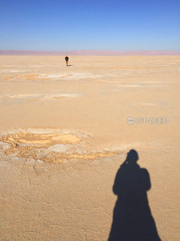 旅行者在干燥的平地上与摄影师的影子走得很远