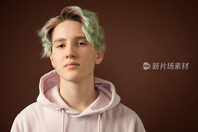 一个十几岁的男孩的工作室肖像与绿色的头发在一个棕色的背景