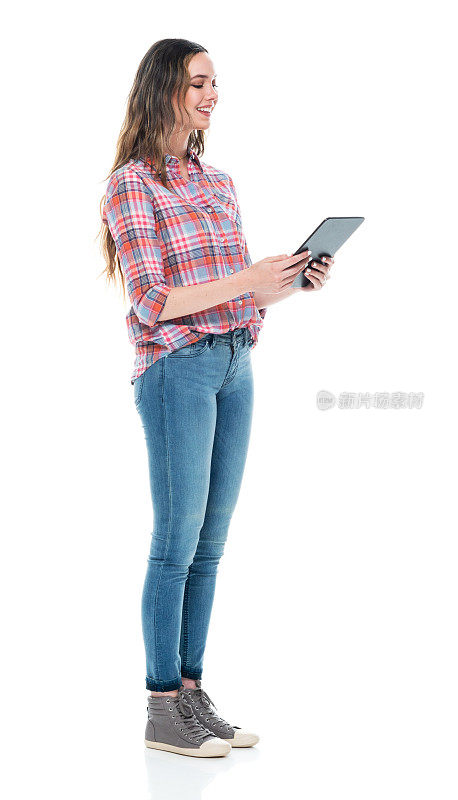 白人女性穿着牛仔裤站在白色背景前使用平板电脑