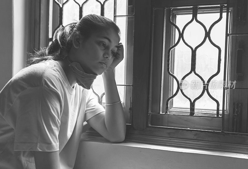 这个悲伤的女孩正在保护自己，戴着口罩，在家里自我隔离。