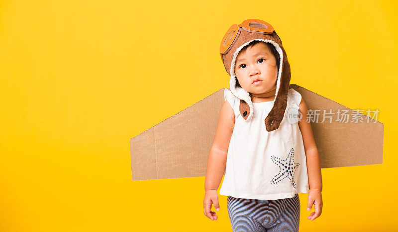 小孩小女孩微笑着戴着飞行员帽玩，护目镜和玩具纸板飞机机翼