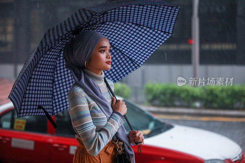 一位戴着头巾、撑着伞的穆斯林马来妇女在雨中行走