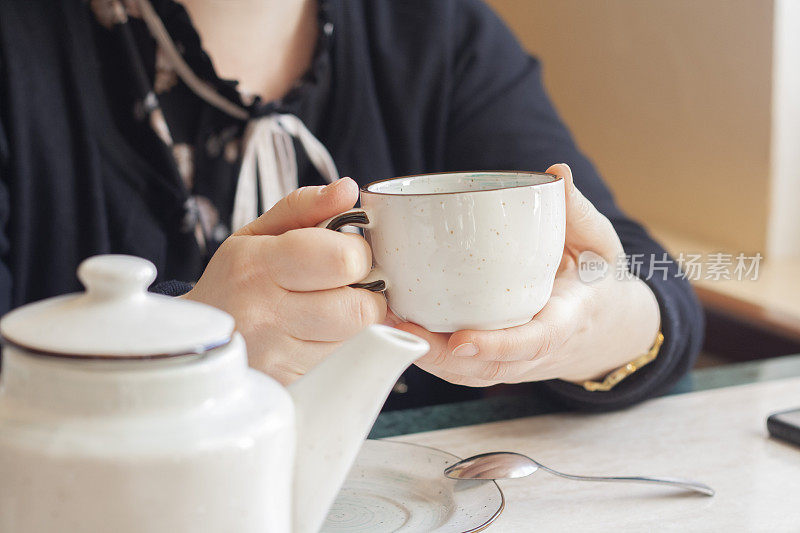 一个女人手里的白杯茶，茶壶，餐厅