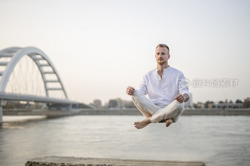 年轻美丽的男子在半空中沉思的肖像，漂浮在户外地面上，坐在莲花姿势，莲花身