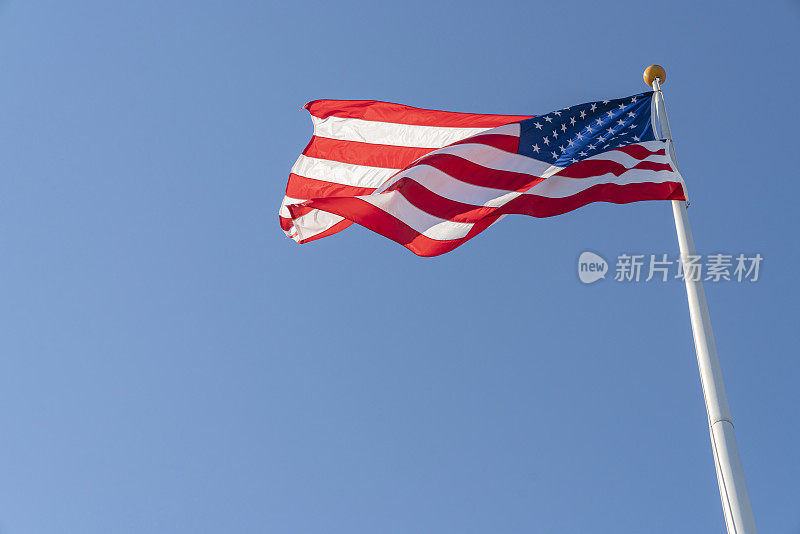 美国国旗飘扬在旗杆上，鲜艳的红白蓝颜色映衬着蓝天