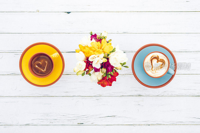 平躺在波西米亚风格的小苍兰和一个黄色和蓝色的杯与奶油咖啡在两杯爱心形状