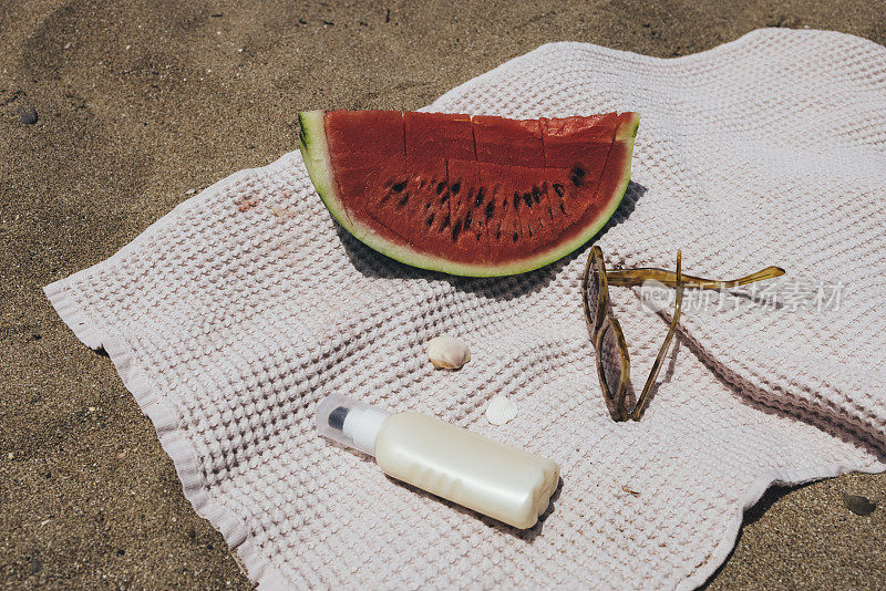 海滩准备好了:海滩上一块西瓜、太阳镜和防晒霜的特写镜头