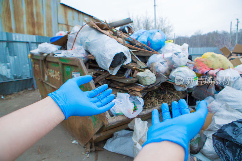 一名男子戴着橡胶手套收集垃圾。容器里有很多垃圾。垃圾崩溃。门卫的罢工。塑料回收的环境灾难。和特写