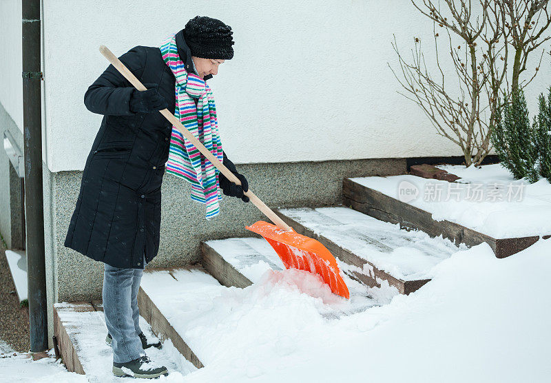 一位中年妇女正在清理屋前的积雪