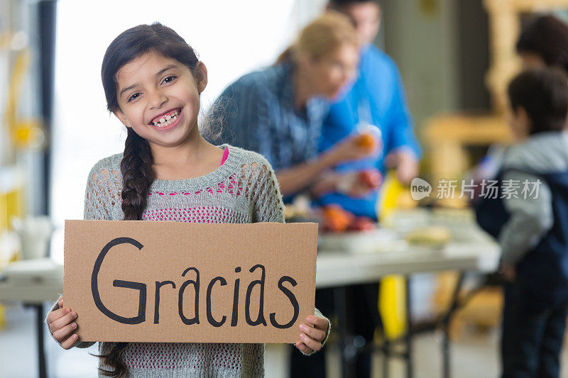 在社区食物银行，快乐的西班牙女孩举着“谢谢”的牌子
