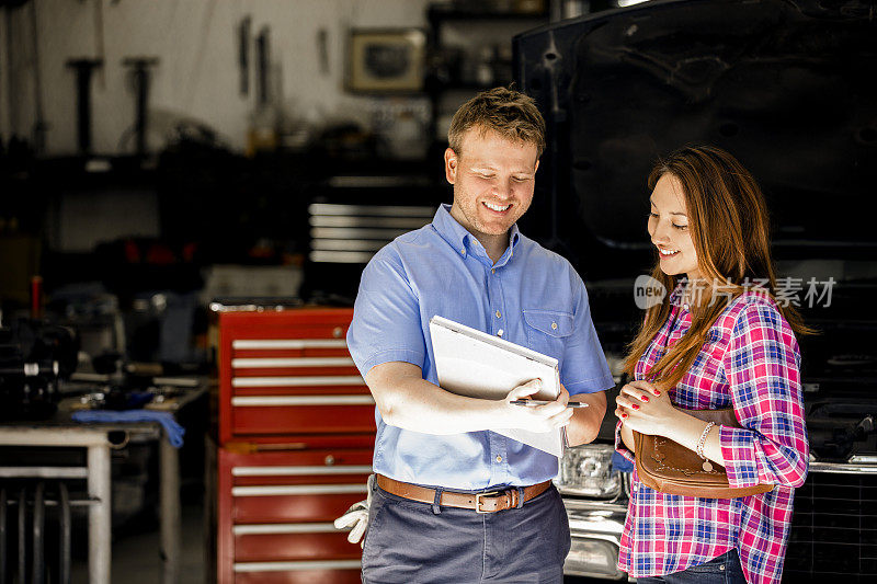 快乐的客户在修理店与汽车修理工讨论修理。