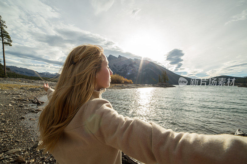 一个年轻女子沿着湖岸走着，双臂伸着
